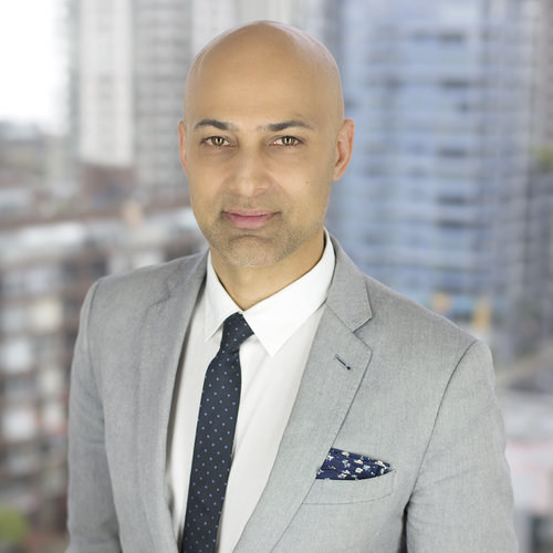 Dr. Paul Waraich wearing grey suit in front of buildings